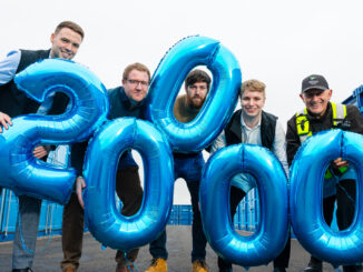 A group of people standing with blue balloons in the shape of £20,000