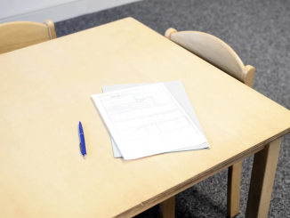 A white exam paper with a pen on a beige desk.